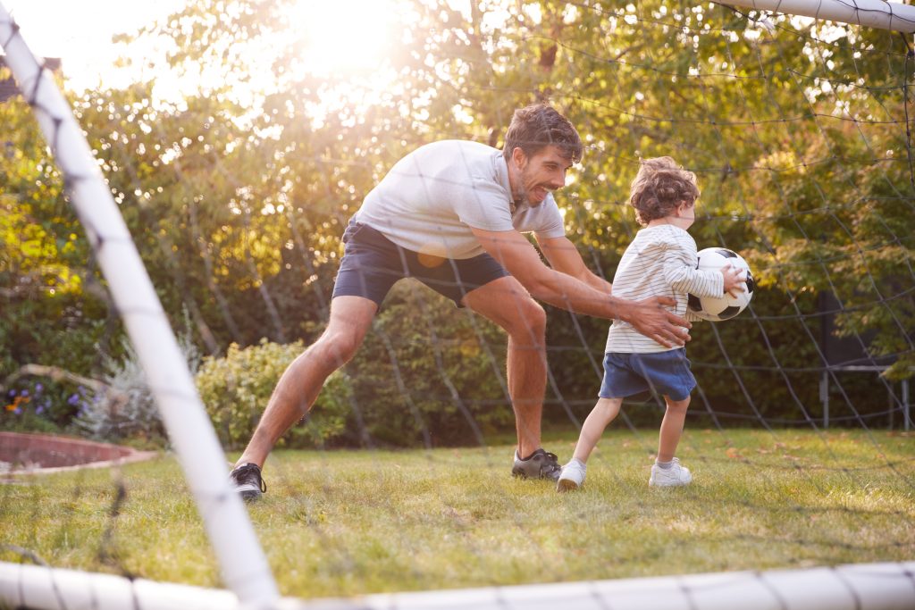 Padre con hijo divirtiéndose en el jardín jugando al fútbol juntos.