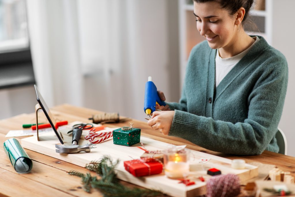 Mujer con pistola de pegamento caliente empaquetando regalo de Navidad DIY en casa.
